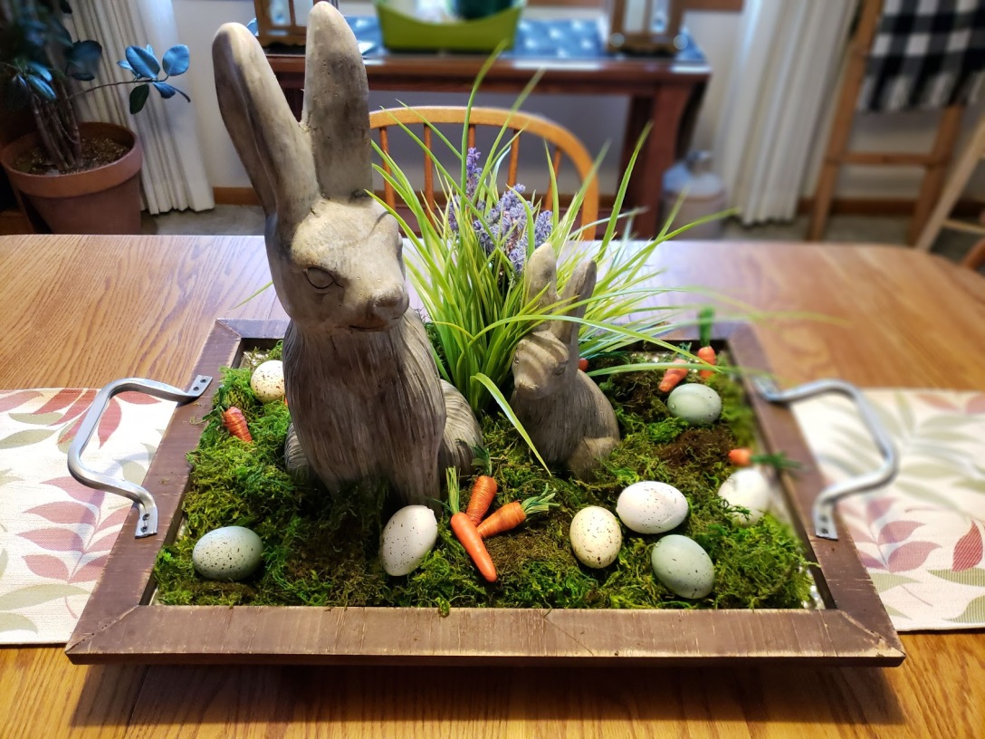 Image of a bunny tablescape. 2 bunnies in a tray with grass and eggs.